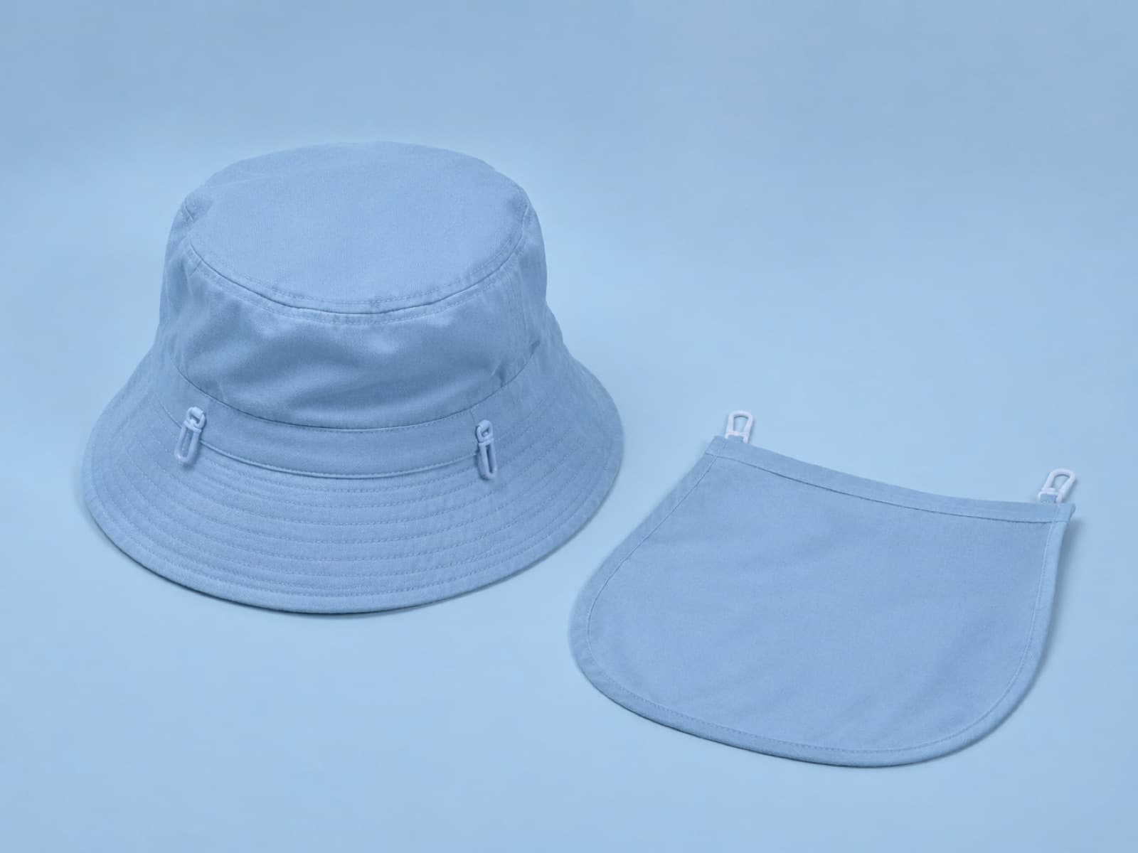 Kids bucket hat with its neck flap unclipped and laid beside it